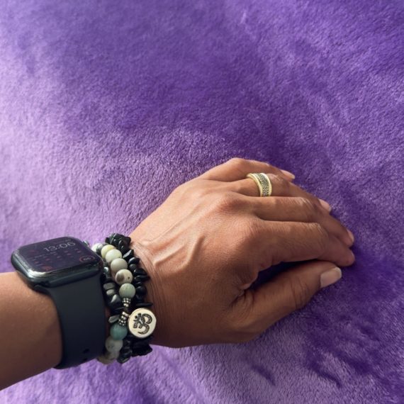 Dahni holistic wellness practitioner has her hand on a client who is Laying underneath a purple blanket, on the therapy Couch/Bed